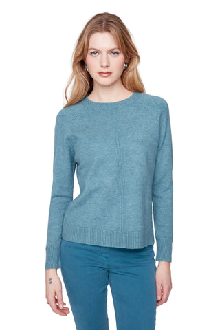 Woman wearing a teal sweater and pants against a white background