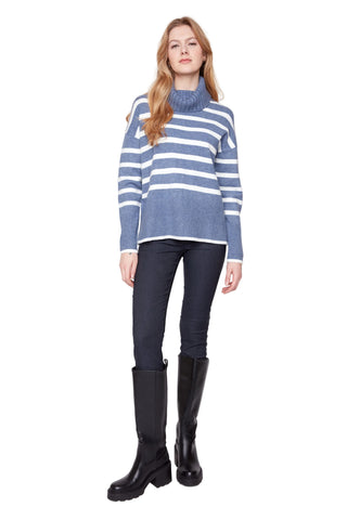 Woman wearing a blue and white striped sweater, black pants, and black boots on a white background