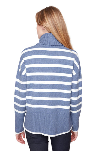 A woman viewed from the back wearing a blue and white horizontally striped knit sweater with a ribbed turtleneck, paired with dark jeans, against a light gray studio background.