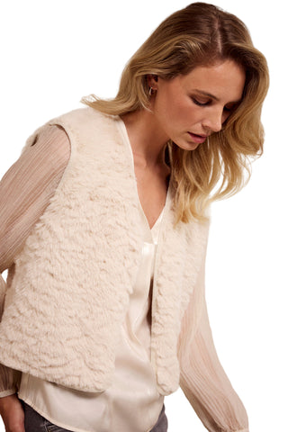 Woman wearing a cream-colored textured vest over a beige shirt against a plain background