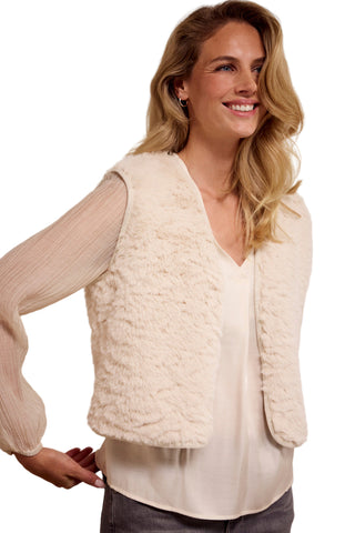 Woman wearing a cream-colored textured vest over a white shirt on a plain background