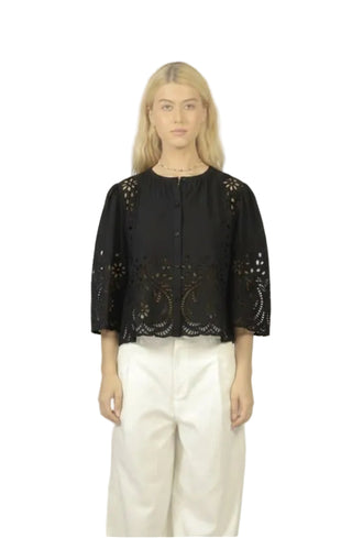 Person wearing a black lace top and white pants on a plain background