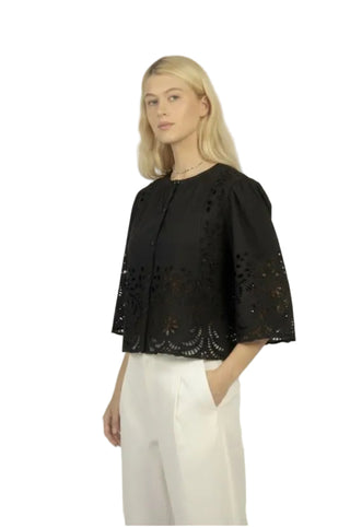 Woman wearing a black lace top and white pants against a plain background