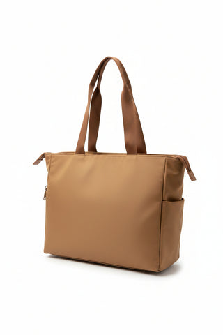 A large tan leather tote bag with brown shoulder straps, displayed on a mannequin wearing a white quilted jacket.