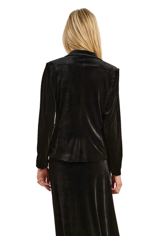 Person wearing a black velvet jacket and skirt set against a beige background