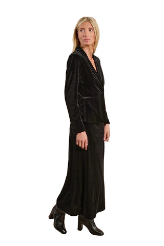 Woman wearing a black velvet outfit with a matching jacket and pants on a beige background
