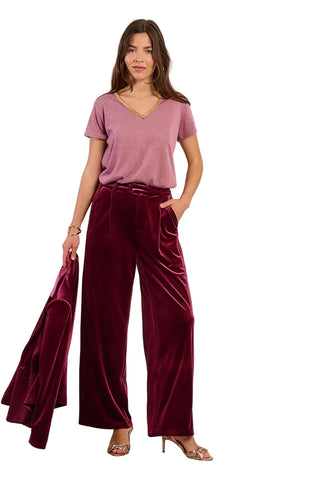 Woman wearing a mauve top and burgundy velvet pants against a beige background