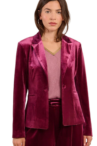 Woman wearing a magenta velvet blazer over a pink top and pants on a beige background