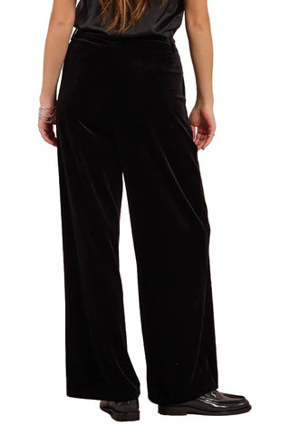 Person wearing black velvet pants against a plain background