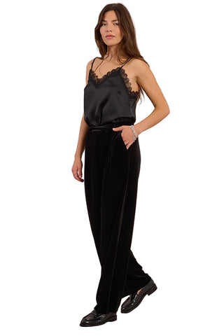 Woman wearing a black satin jumpsuit with lace detailing on a pink background