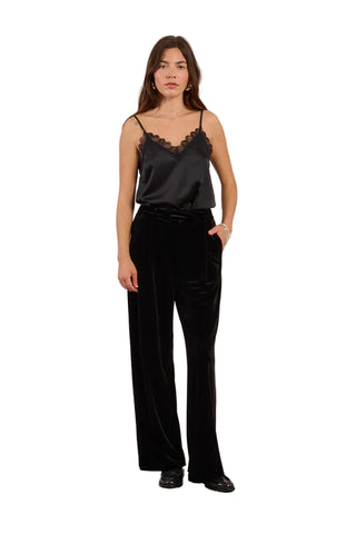 Woman wearing a black satin camisole and black wide-leg pants against a beige background