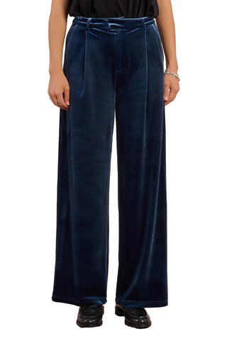 Navy velvet pants worn by a person on a pink background