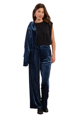 Woman wearing a blue velvet outfit with a black top against a beige background