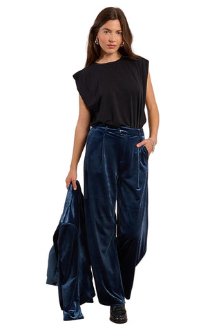 Woman wearing a black top and blue velvet pants against a beige background