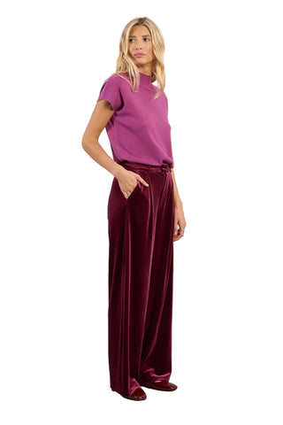 Woman wearing a purple top and burgundy velvet pants on a beige background