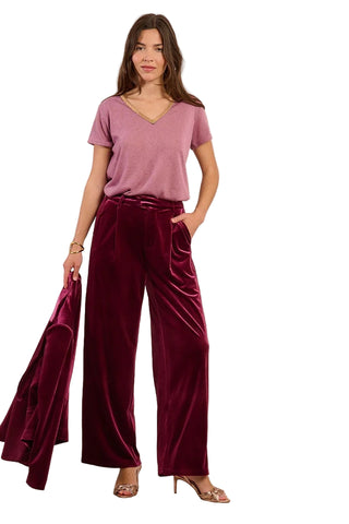 Woman wearing a mauve top and burgundy velvet pants against a beige background