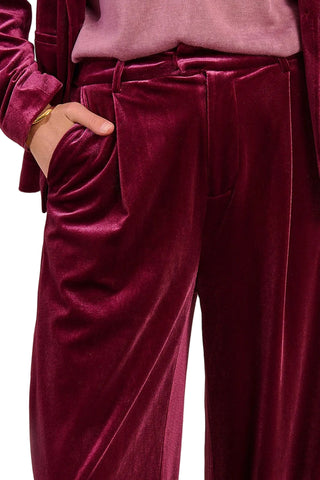 Maroon velvet pants worn with a pink top on a neutral background