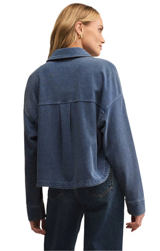 Person wearing a blue denim jacket and jeans on a beige background