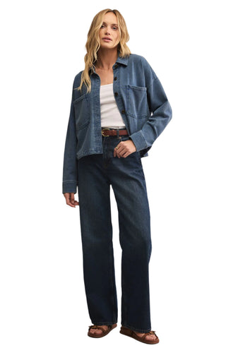 Woman wearing a blue denim jacket and jeans on a beige background