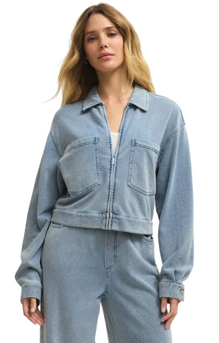 Woman wearing a light blue denim jacket and pants on a plain background