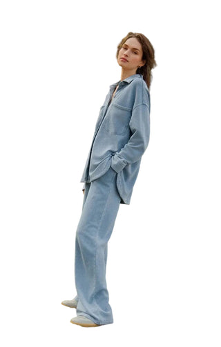 Woman in a light blue outfit standing in a park with trees and a building in the background