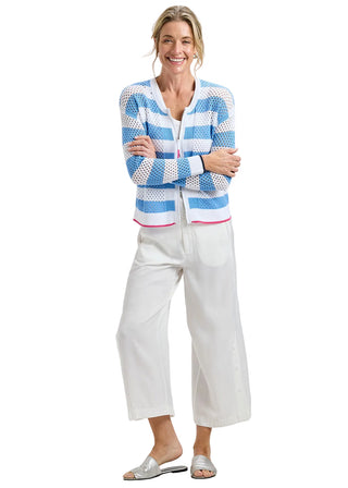 Woman wearing a blue and white striped cardigan with white pants on a plain background