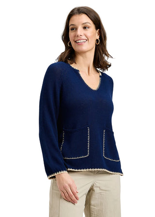 Woman wearing a navy blue sweater with beige trim on a gray background