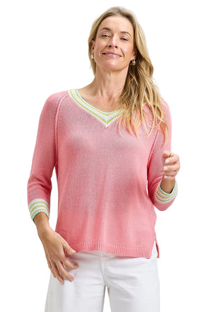 Woman wearing a pink sweater with decorative trim on a plain background