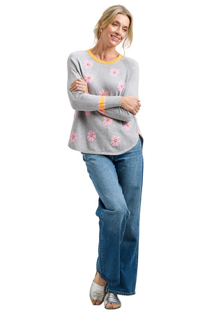 Woman wearing a gray sweater with floral patterns and blue jeans on a white background