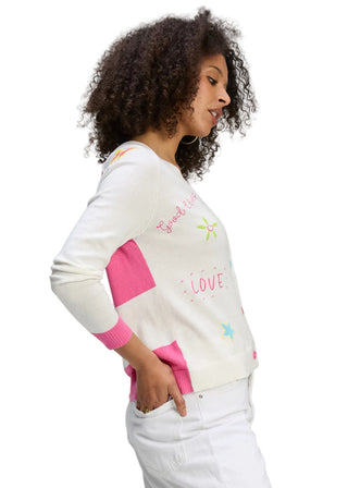 Woman wearing a white sweater with pink sleeves and colorful text on a gray background