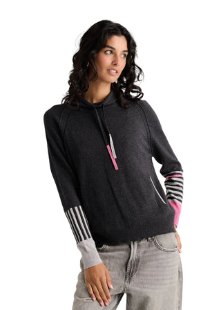 A woman wearing a dark charcoal gray knit hoodie with pink and white striped sleeve details, paired with light gray jeans, against a plain light gray background.