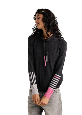 A woman wearing a dark gray heathered pullover hoodie with pink and white striped sleeve cuffs, paired with light gray jeans, against a plain light gray background.