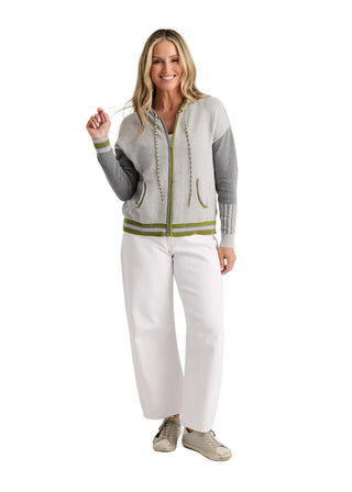 A woman modeling a light gray zip-up cardigan with olive green trim and white wide-leg pants, standing against a plain light gray studio background.