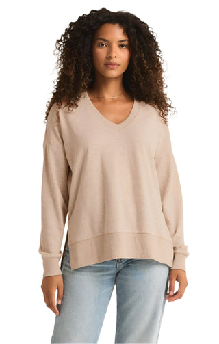 Woman wearing a beige sweater and light blue jeans against a plain background