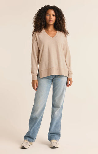 Woman wearing a beige sweater and blue jeans on a plain background