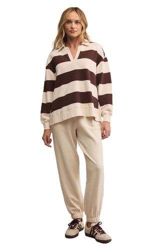 Woman wearing a brown and white striped sweater with cream pants on a beige background
