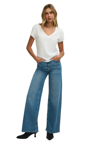 Woman wearing a white t-shirt and blue jeans against a plain background