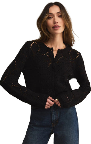 Woman wearing a black lace cardigan and blue jeans against a beige background