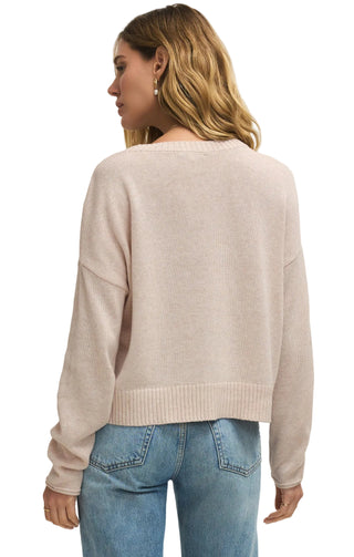 Woman wearing a light pink sweater and blue jeans on a plain background