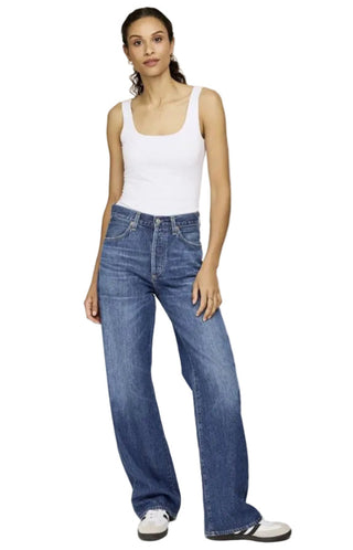 Woman wearing a white tank top and blue jeans on a plain background