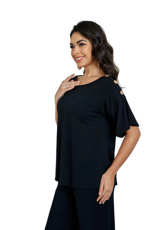 Woman wearing a black outfit with shoulder embellishments in a bright room.