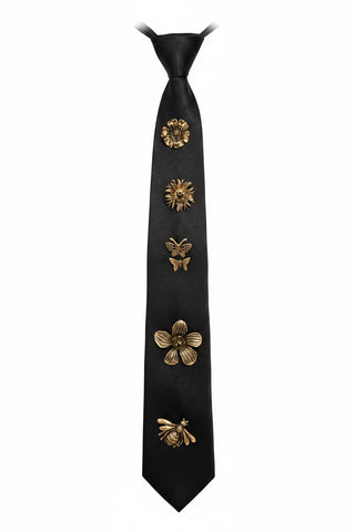 A black necktie displayed on a black mannequin torso, decorated with five metallic gold embroidered motifs including flowers, butterflies, and a bee along the center. The background features a textured metallic silver circular pattern.