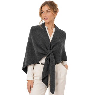 A woman modeling a dark gray knitted wrap poncho tied at the waist, worn over a white collared shirt and cream trousers against a plain white studio background.