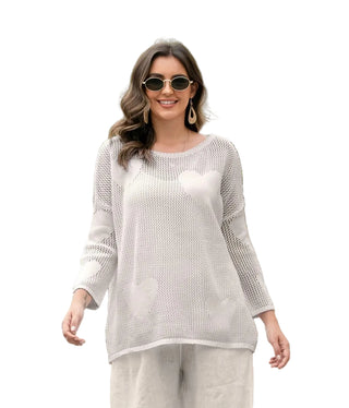 Woman wearing a white lace top and pants outdoors with greenery in the background