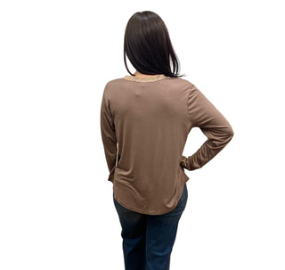 Person wearing a brown long-sleeve top and blue jeans standing in front of a white curtain.