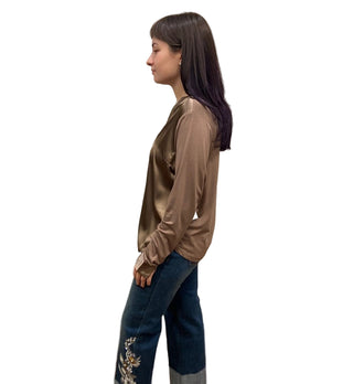 Person wearing a brown satin top and blue jeans with floral embroidery in a fitting room.