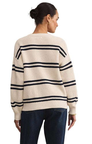 Woman wearing a cream sweater with navy stripes on a beige background