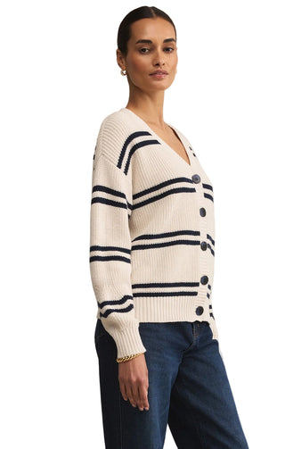 Woman wearing a white sweater with black stripes and buttons on a beige background