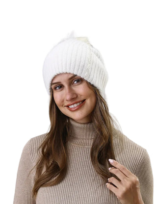 Woman wearing a white knit beanie and beige turtleneck sweater against a light gray wall.