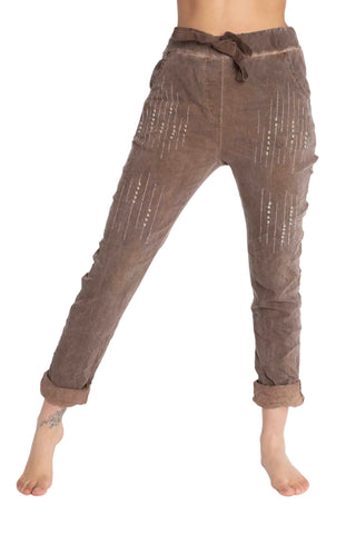 Brown linen pants with vertical slit details and small bead embellishments, shown on a model from the waist down against a white background.